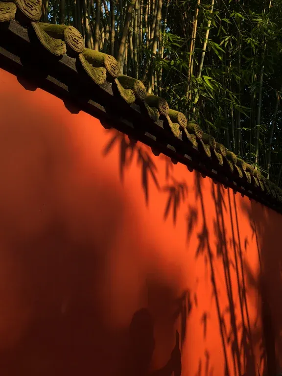 Curving vermilion wall corridor at Wuhou Shrine with bamboo shadows in late afternoon sunlight